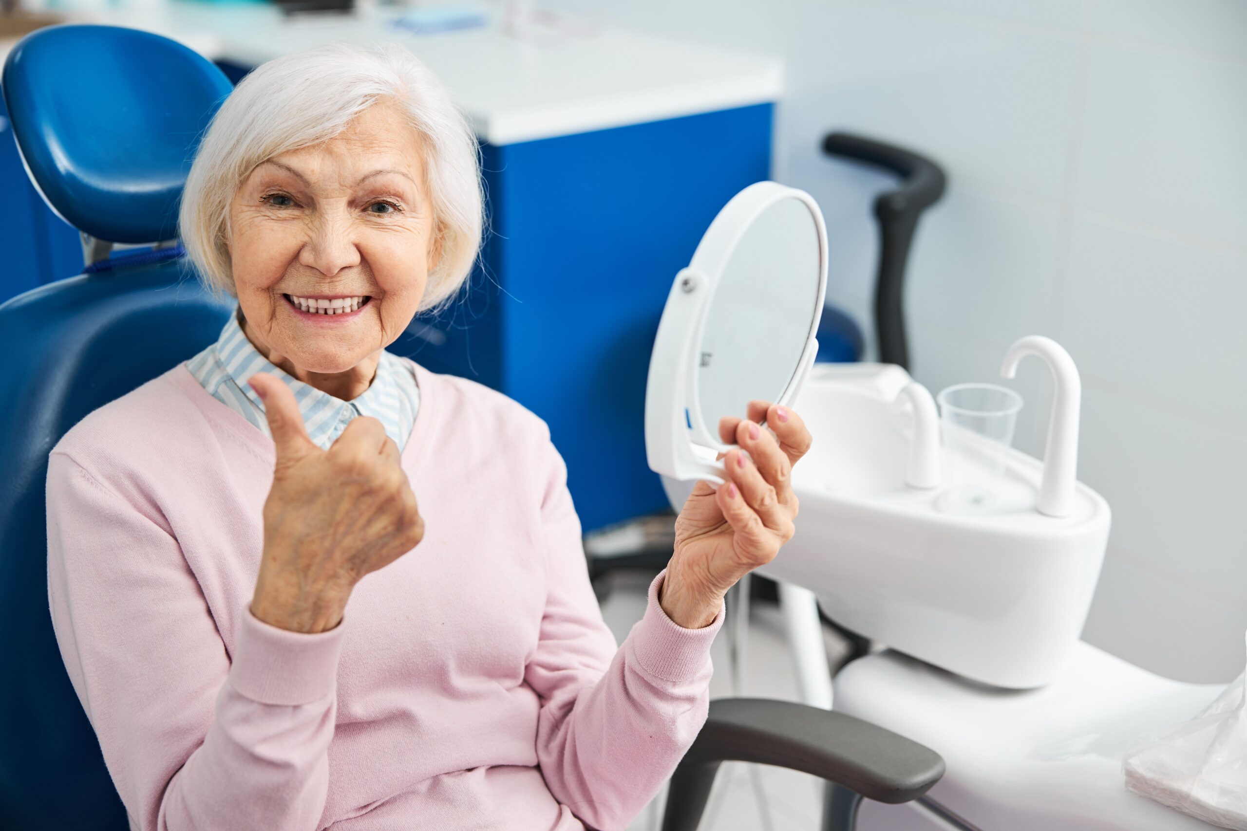 Older woman checking her smile in a mirror after dental treatment
